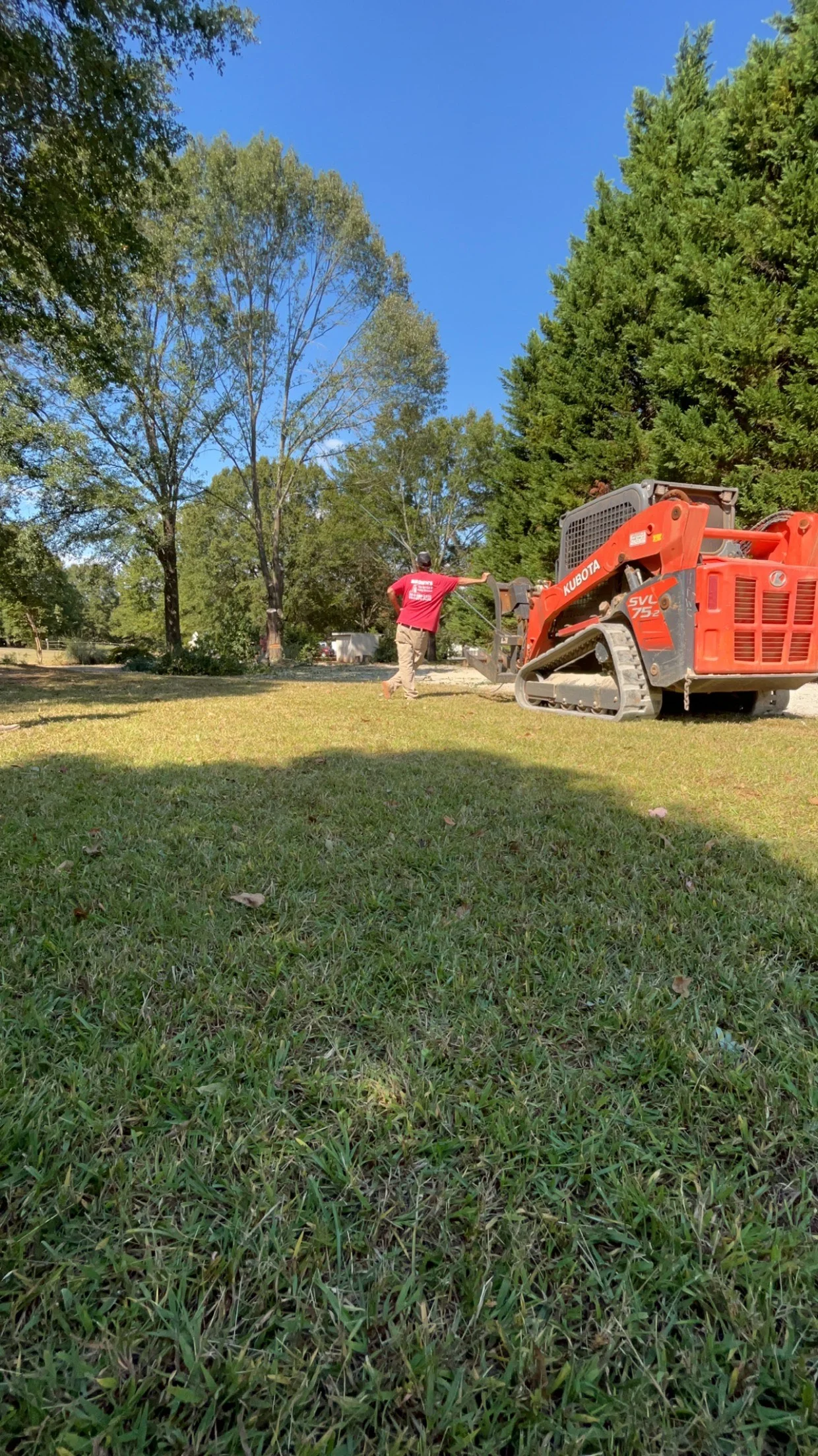 Kubota tracked skid steer loader removing tree debris from cleared residential lot with mature trees