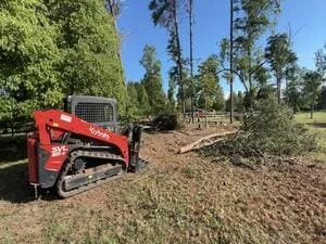 Red tracked skid steer with wood chipping attachment processing tree debris on cleared land
