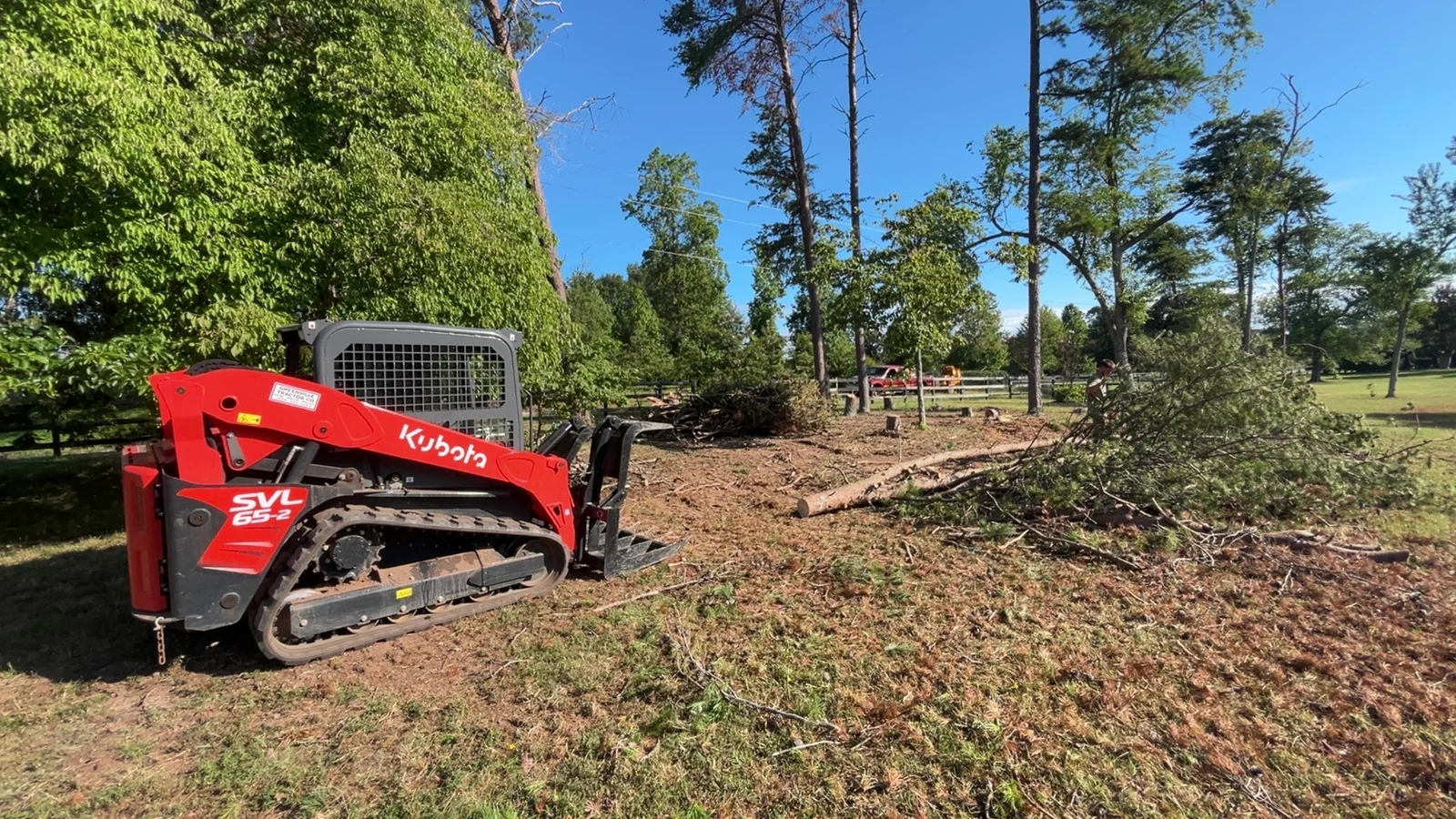 Red Kubota track loader clearing fallen trees and brush from wooded property